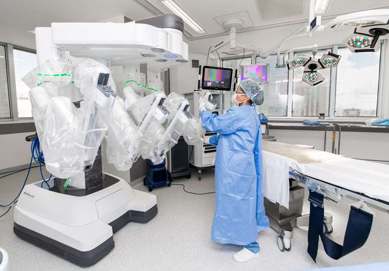 Médico na sala cirúrgica com o robô da Vinci durante procedimento cirúrgico.