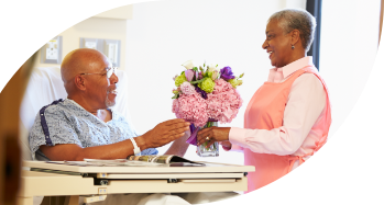 Imagem de um paciente na cama de um hospital recebendo flores de uma mulher