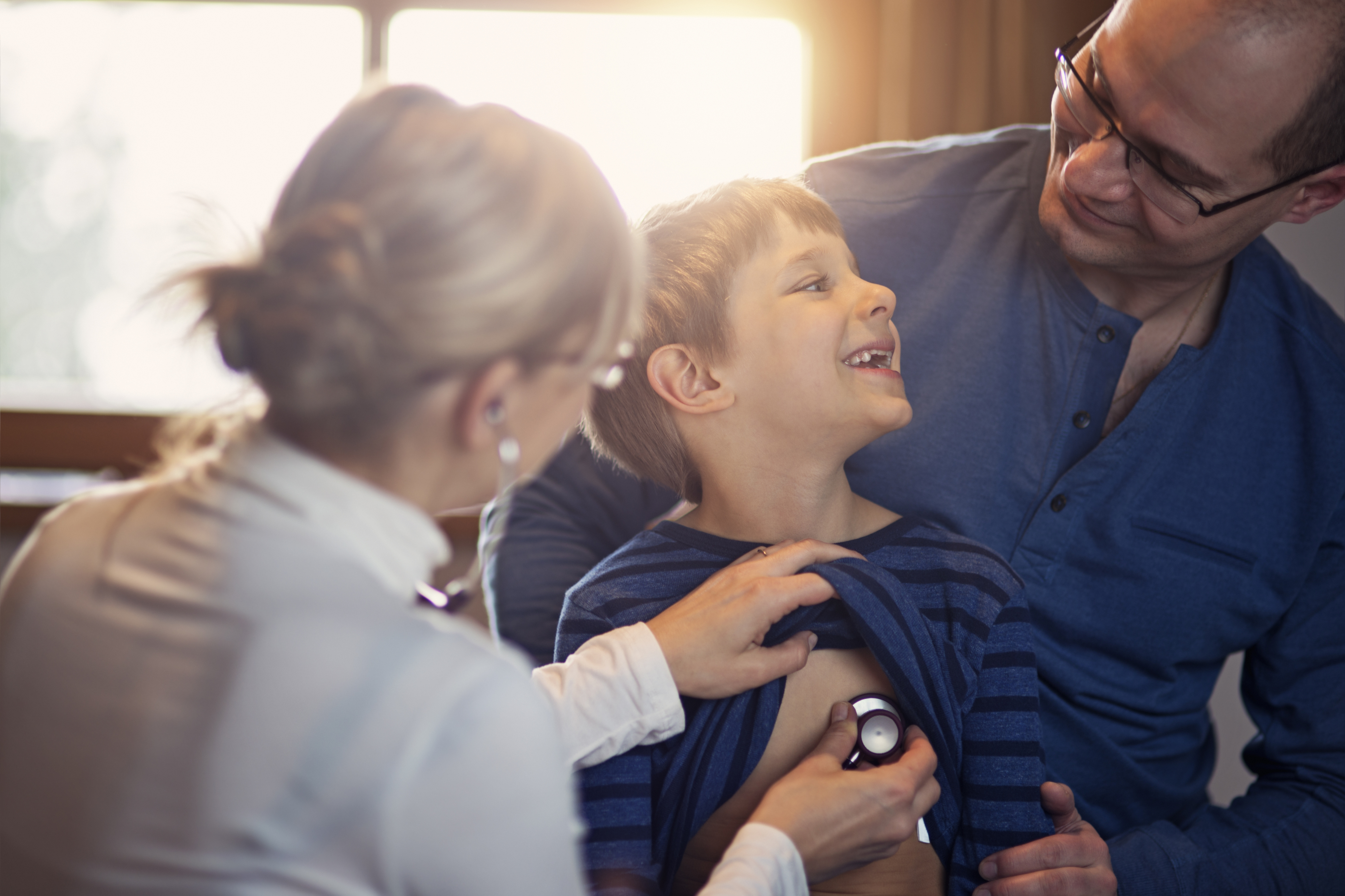 Criança sorri enquanto é examinada pela pediatra na companhia do pai