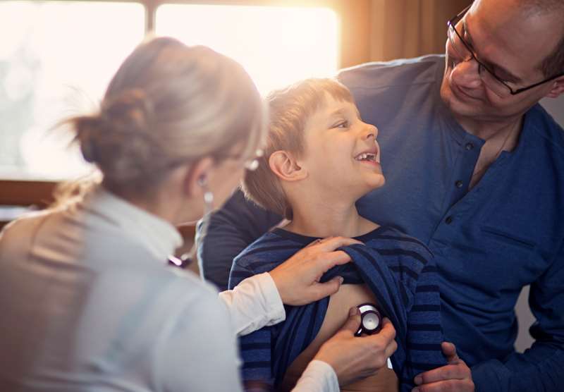 Criança sorri enquanto é examinada pela pediatra na companhia do pai