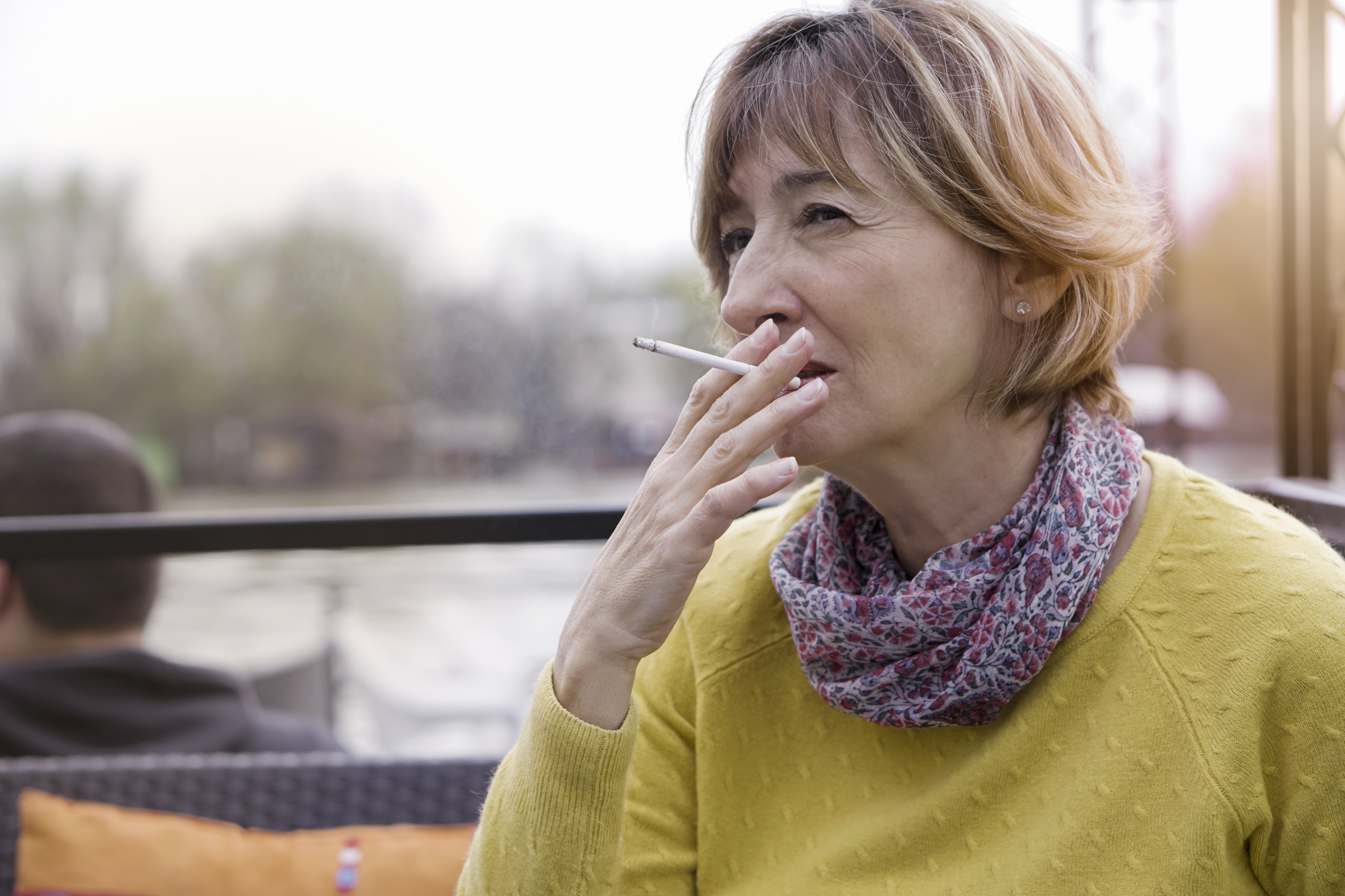 Mulher segurando um cigarro em uma área externa.