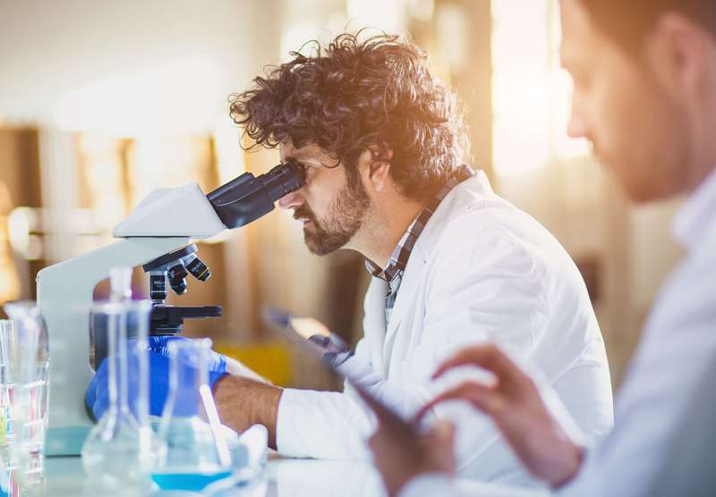 Médicos analisam material no microscópio e fazem anotações em laboratório.