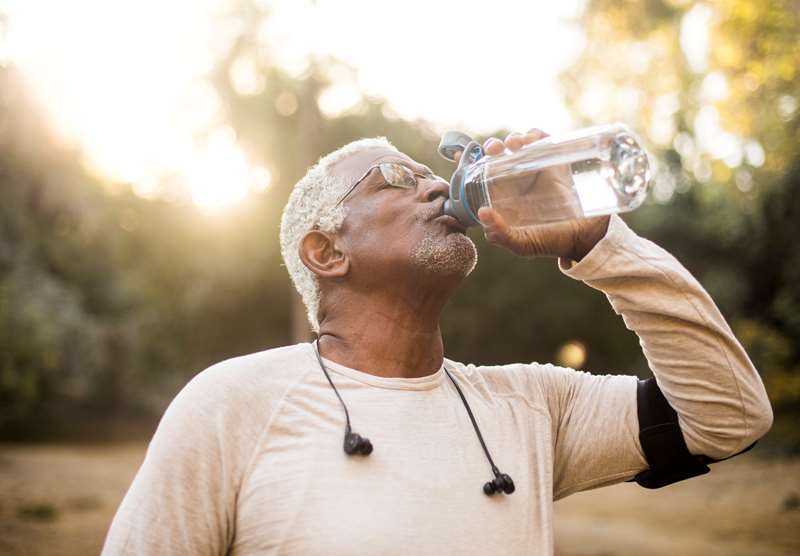 Homem maduro bebe água após prática de atividade física ao ar livre.