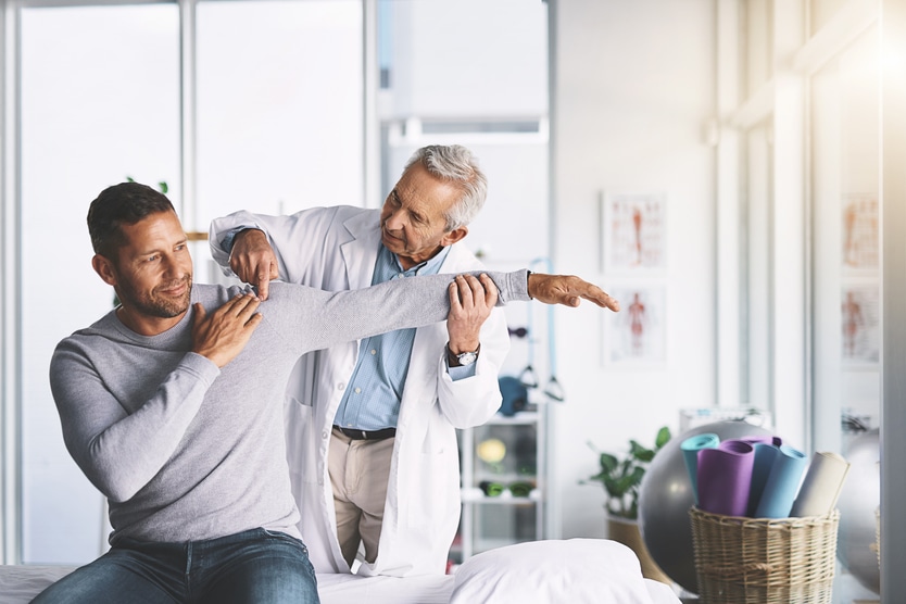 Médico examina ombro de paciente.